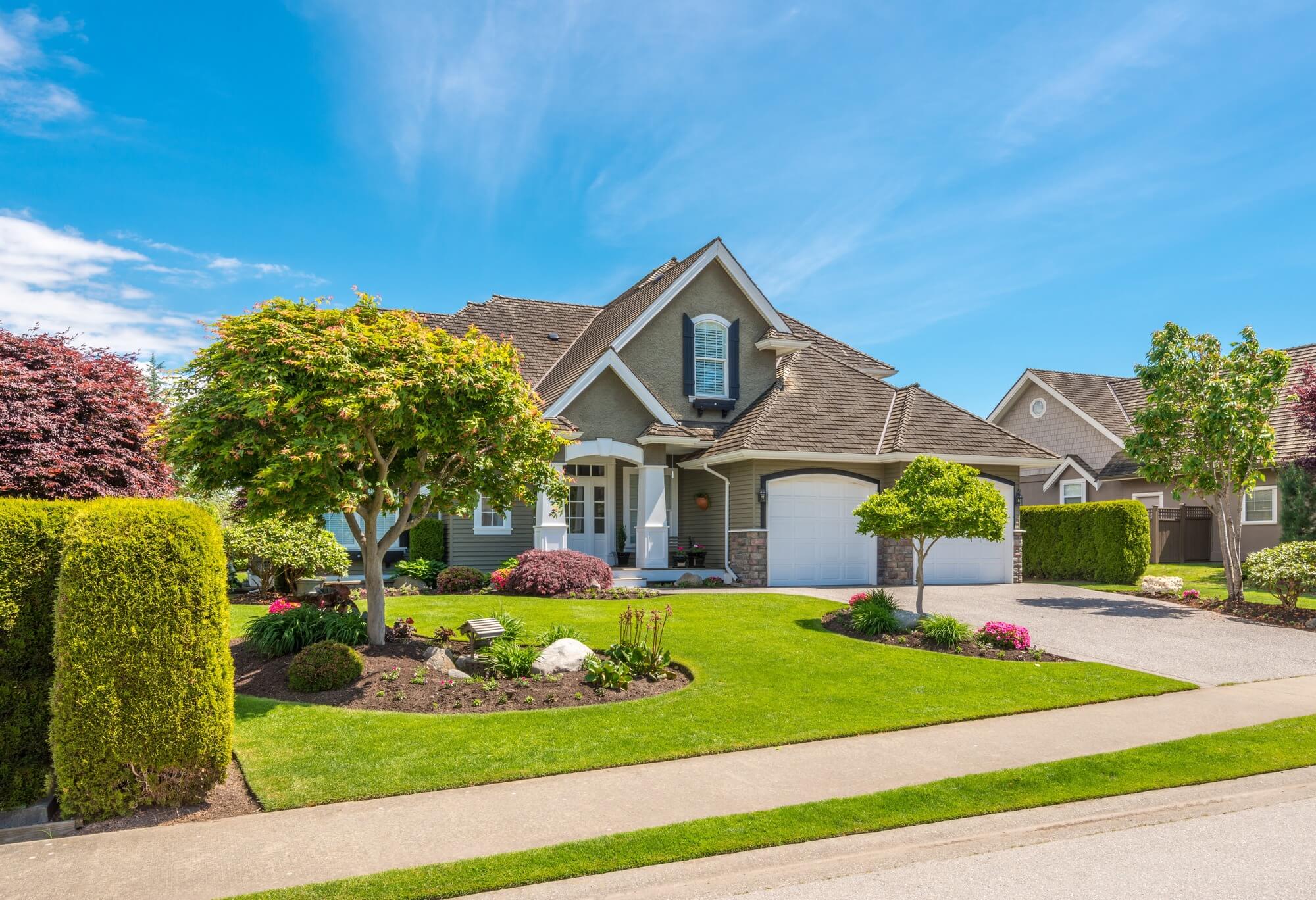 Front exterior of a two-story suburban home with a manicured lawn and landscaped garden beds